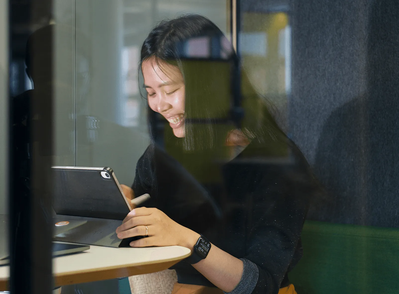 Lisha smiling while drawing on an iPad in a glass meeting room